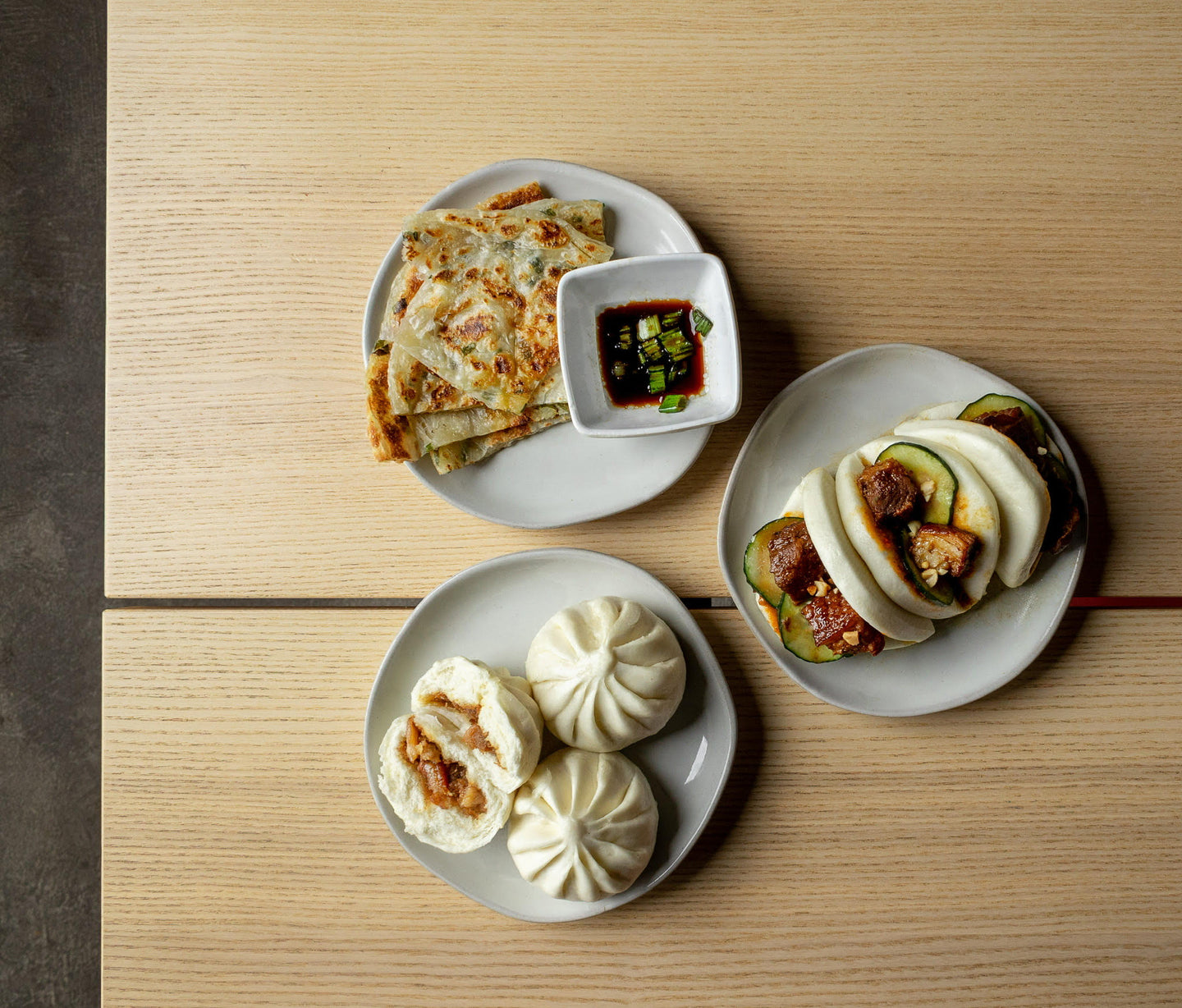 Food lineup from Spring 2023 including Spring Onion Pancakes with a side of soy sauce, Steamed Buns, and Pork Belly Bao Buns.